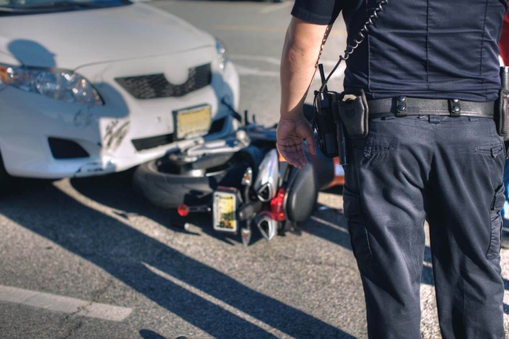 An officer standing in front of a car and motorcycle accident on the road 