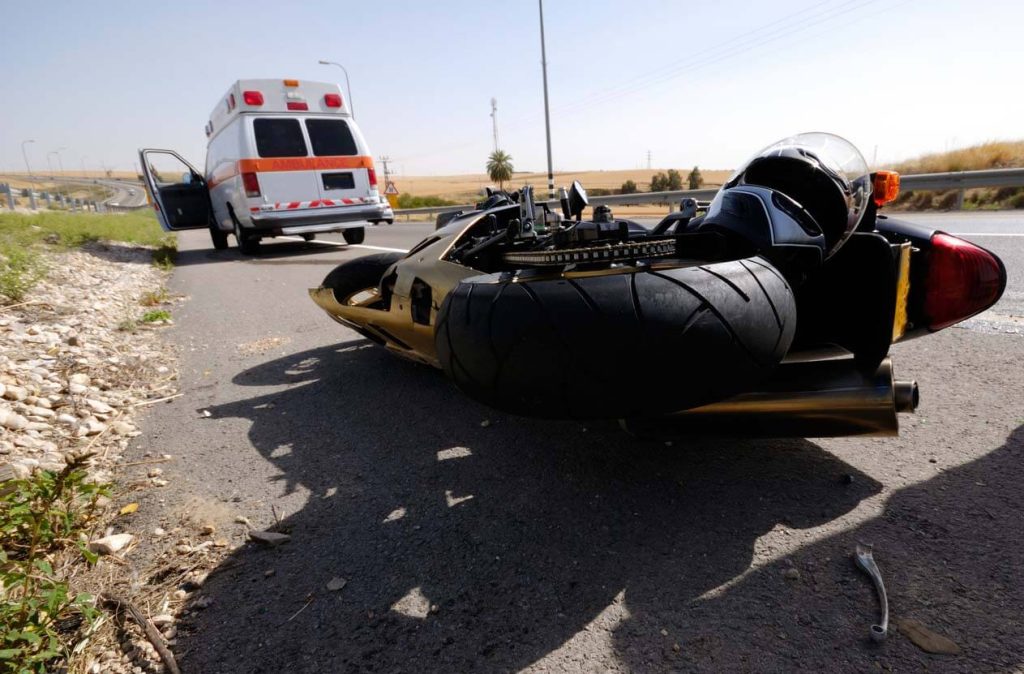 an ambulance arriving to a motorcycle accident scene with the motorcycle on the ground