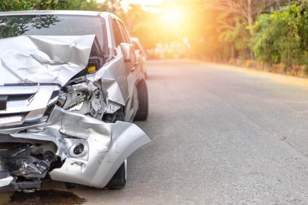 a grey car that has severe front damage parked on the side of a road after a car accident
