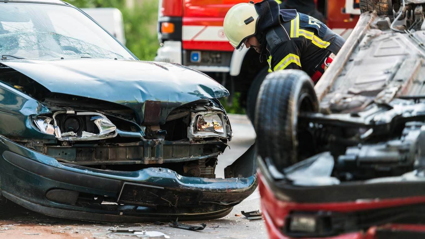 a fireman inspecting two cars that are severely damaged after a car accident