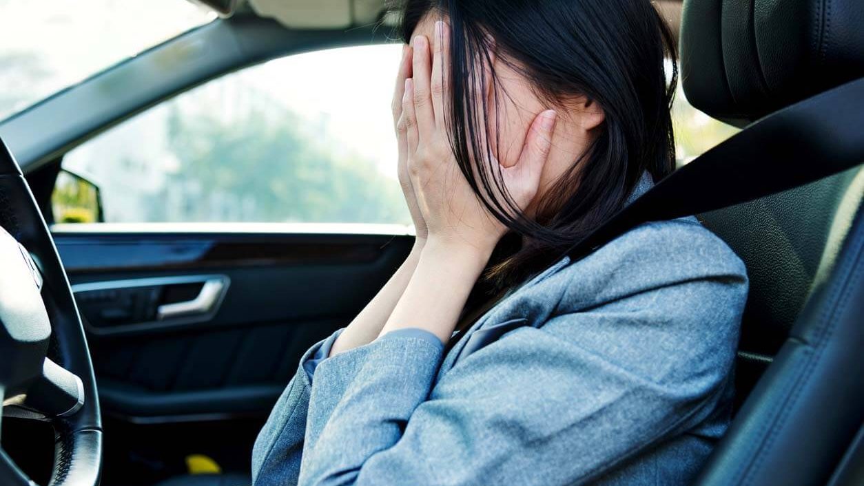 a woman crying in her car with her face covered after getting into a car accident and realizing she needs to call a car accident lawyer