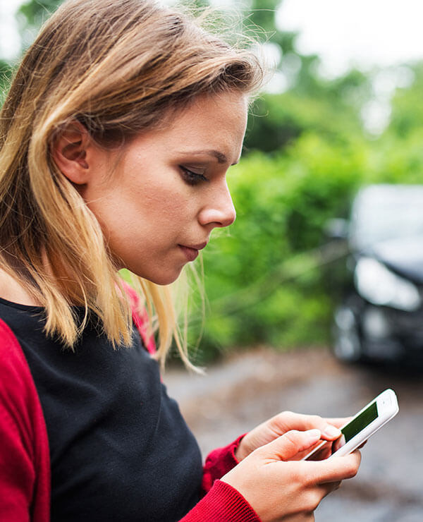 woman by car wreck contacting Kansas City Car Wreck Lawyers on her smart phone